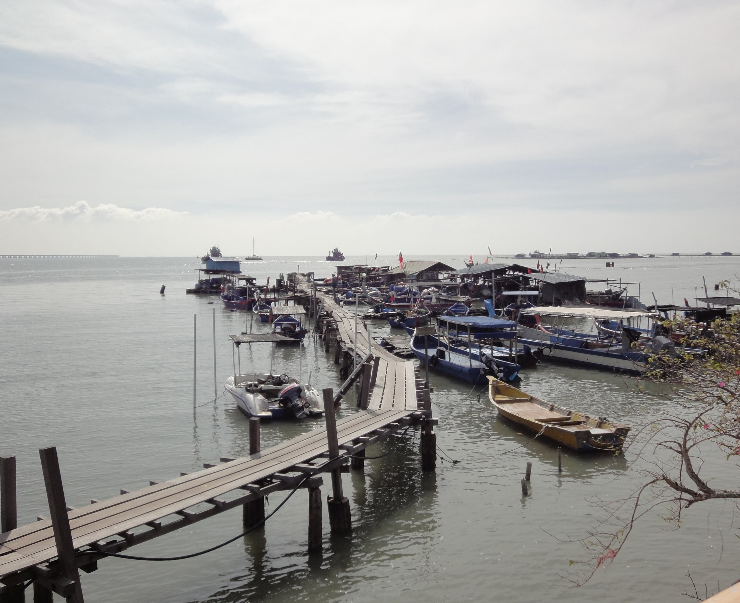 A timber fishing jetty on stilts at Batu Maung, with moored fishing boats and sheds