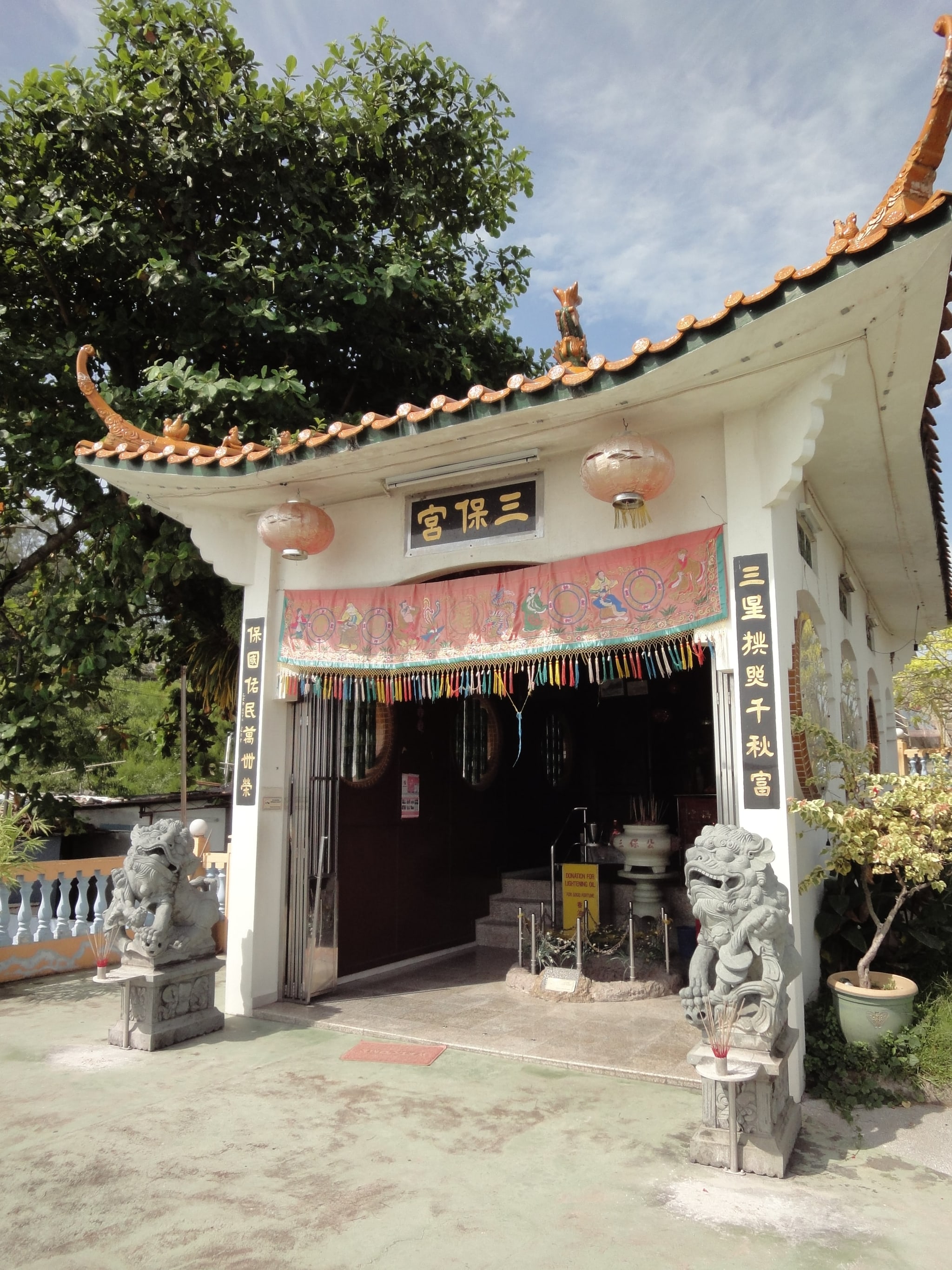 The small Sam Poh temple at Batu Maung, with an orange-tiled roof and stone guardian lions at its door